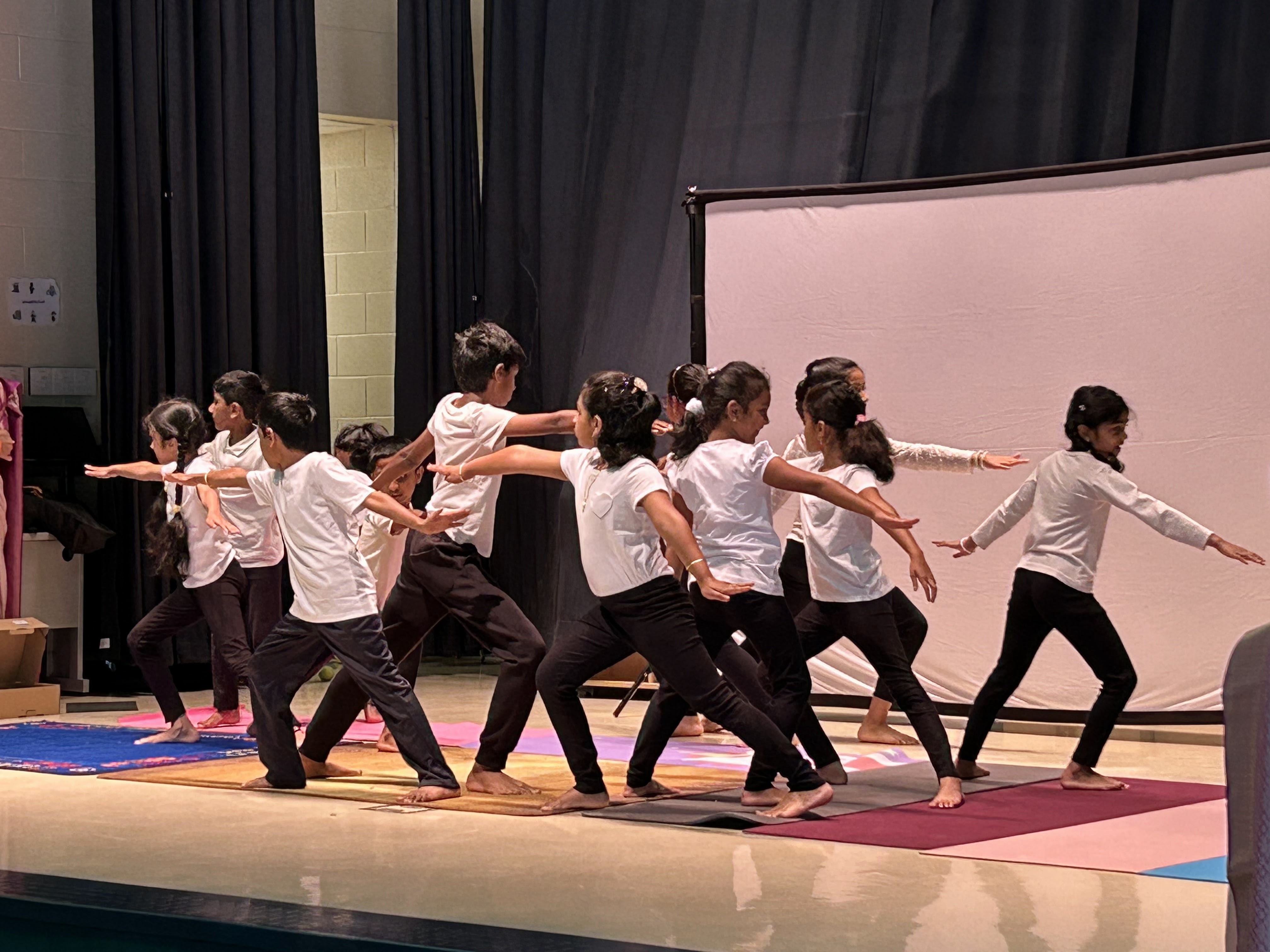 Prajna students in synchronized Warrior II yoga pose on stage
